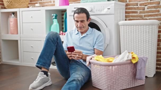中年男子在洗衣房用智能手机等洗衣机 — 图库视频影像