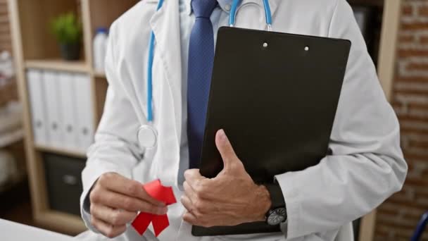 Young Hispanic Man Doctor Holding Red Ribbon Clipboard Clinic — Stock Video