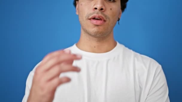 孤立した青い背景の上に考える深刻な表現で立っている若いラテン人男性 — ストック動画