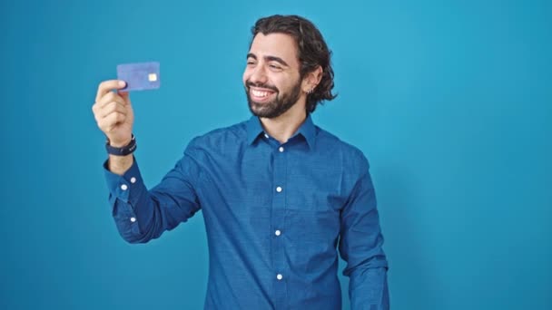 年轻的惊慌失措的男人带着自信的笑容 拿着信用卡庆祝孤立的蓝色背景 — 图库视频影像