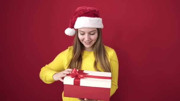 Young Blonde Woman Wearing Christmas Hat Unpacking Gift Isolated Red — Stock Video