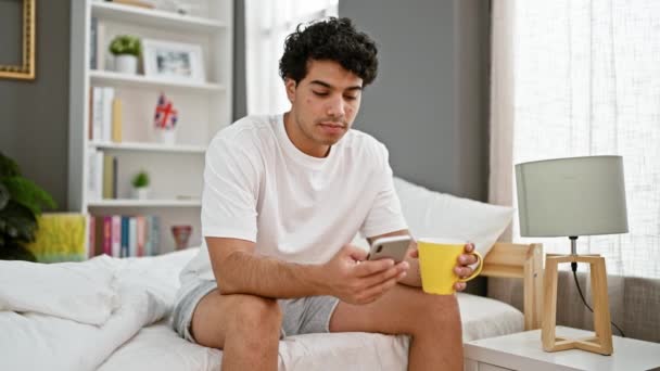 Joven Latino Usando Smartphone Bebiendo Café Dormitorio — Vídeos de Stock