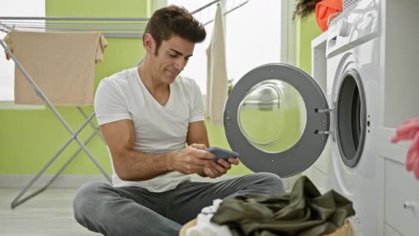 年轻人在洗衣房里玩电子游戏 洗衣服时面带微笑 — 图库视频影像