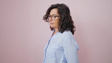 Middle age hispanic woman standing with serious expression over isolated pink background
