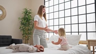 Mutlu beyaz anne ve kız birlikte, gülümseyerek ve yatakta rahat bir şekilde oturarak, rahat bir yatak odasında oyuncaklarla oynayarak, ev yaşamlarının tadını çıkararak..