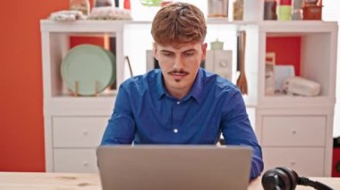 Sofrada oturmuş gülümseyen dizüstü bilgisayar kullanan İspanyol bir genç.