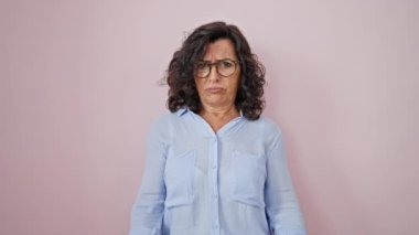 Orta yaşlı İspanyol bir kadın öfkeli bir ifadeyle izole edilmiş pembe arka planda orta parmak hareketi yapıyor.