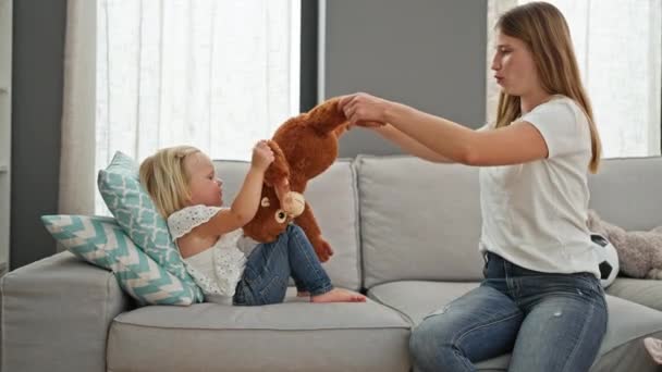 ハッピーな白人のお母さんと小さな娘は快適にソファーでリラックスして 家で居心地の良いリビングルームで猿人形と一緒に遊んでいます — ストック動画