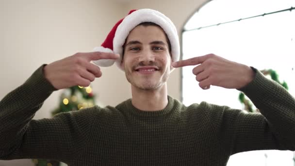 若いヒスパニックの男は 自宅でクリスマスツリーで立って口を指して指を指して — ストック動画