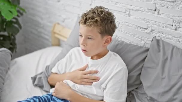 可爱的金发男孩 穿着睡衣坐在床上 一大早咳嗽起来 生病的孩子躺在卧室里 与流感作斗争 呆在舒适的房子里 — 图库视频影像