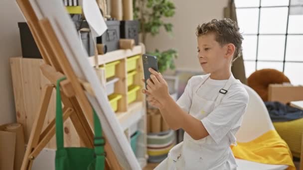 美しいブロンドの少年アーティスト 彼は芸術スタジオで写真を撮っているように微笑んで キャンバスに彼の傑作を描く準備ができています — ストック動画