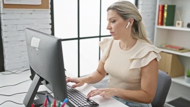 オフィスで笑顔のコンピュータとイヤホンを使用して若い金髪女性ビジネスワーカー — ストック動画