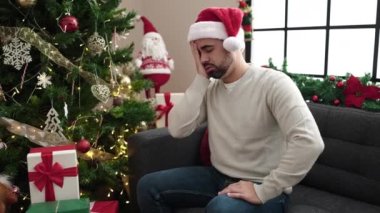 Kafası ve midesi ağrıyan İspanyol genç adam Noel ağacının yanında oturuyor.