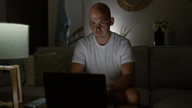 Genç İspanyol adam dizüstü bilgisayar kullanıyor. Kanepede oturmuş kutlama yapıyor.