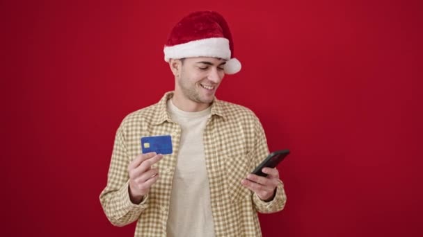 年轻的他的惊慌失措的男人用智能手机在孤立的红色背景下进行圣诞网上购物 — 图库视频影像