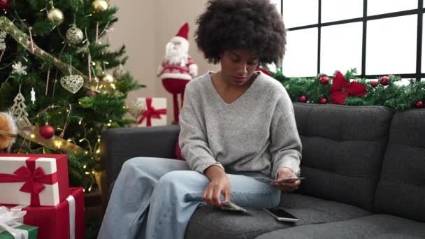 アフリカ系アメリカ人女性 自宅でクリスマスツリーでスマートフォンを使ってドルを数える — ストック動画