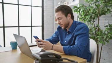 Ofiste kutlama yapmak için dizüstü bilgisayar ve akıllı telefon kullanan İspanyol bir iş adamı.