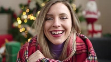 Evdeki Noel ağacının yanında kendinden emin gülümseyen genç sarışın kadın.