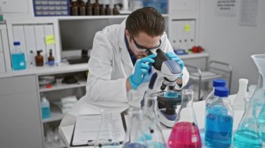 Genç İspanyol bilim adamı laboratuarda mikroskop kullanarak rapor yazıyor.