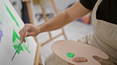 Yakışıklı genç İspanyol bir adam, hevesli bir sanatçı, resim stüdyosunun kalbinde tutkulu bir şekilde resim çiziyor, boya fırçası elini dikkatlice tutuyor.