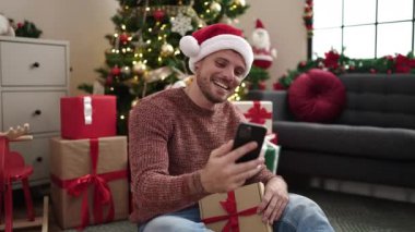 Kafkasyalı genç bir adam evdeki akıllı telefonuyla bir video görüşmesinde hediye gösteriyor.
