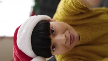 Genç Çinli bir kadın evde Noel şapkası takıyor.