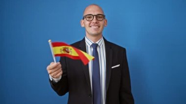 İspanya bayrağı taşıyan genç İspanyol iş adamı izole edilmiş mavi arka planda gülümsüyor.