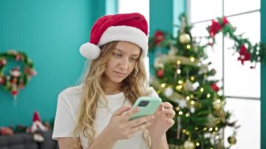 Genç sarışın kadın akıllı telefon kullanarak Noel 'i evde kutluyor.