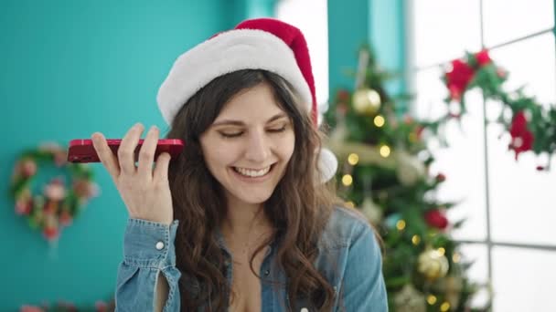 自宅でクリスマスを祝うスマートフォンで音声メッセージを聞く若い美しいヒスパニックの女性 — ストック動画