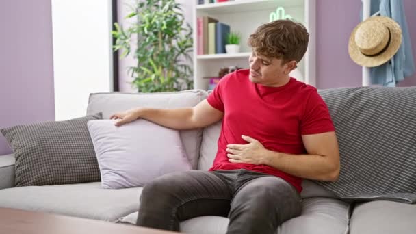 重度の胃痛に苦しむ若いヒスパニック系男性が アパートのリビングルームのソファーで休んでいる間 不幸にも腹部に触れ 屋内病の絵を描いている — ストック動画