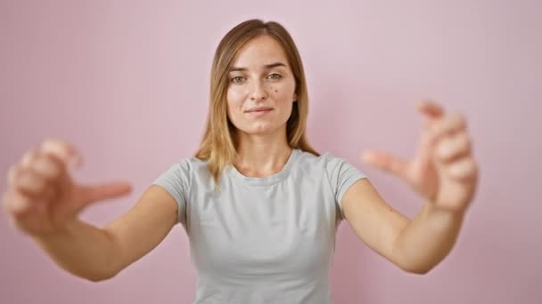 쾌활한 금발의 여자는 자신감으로 손으로 기호를 분홍색 배경에 캐주얼 포즈를 — 비디오