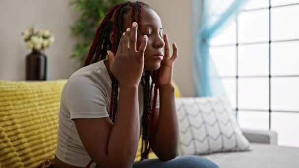 忧心忡忡的非洲裔美国女人 辫子独自坐在沙发上 愁眉苦脸 露出头痛和压力 — 图库视频影像