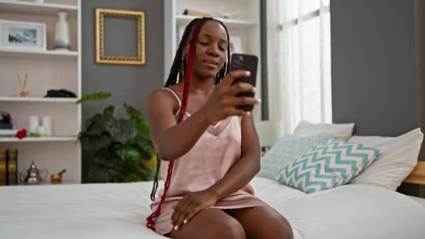 一个有着辫子的快乐的非洲裔美国女人 在舒适的床上愉快地打了个电话打招呼 在她舒适的公寓卧室里享受着在线交流 — 图库视频影像