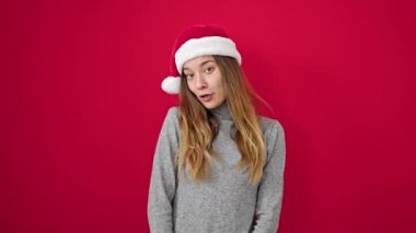 Kafkasyalı genç bir kadın kendine güvenen, izole kırmızı arka planda bir Noel şapkası takan.