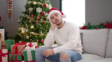 Genç İspanyol adam Noel şapkası takıyor ve eve üzgün bakıyor.