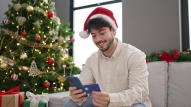 Genç İspanyol adam akıllı telefon ve kredi kartıyla evde Noel 'i kutluyor.