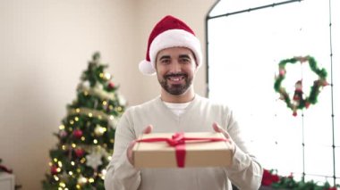 Evdeki Noel ağacının yanındaki koltukta oturan İspanyol genç adam hediyesini tutuyor.