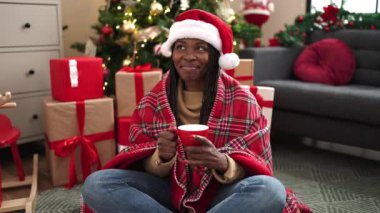 Afrikalı kadın evde Noel ağacının yanında kahve içiyor.