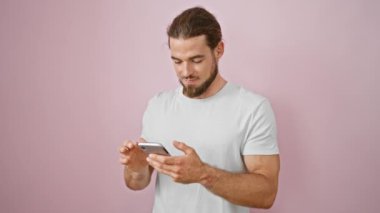 Genç İspanyol adam akıllı telefon kullanıyor, pembe arka planda gülümsüyor.