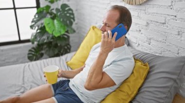 İspanyol orta yaşlı bir adam rahat yatak odasında rahat rahat pijamalarını giyiyor, sabah kahvesini yudumlarken akıllı telefonuyla ciddi bir konuşma yapıyor..