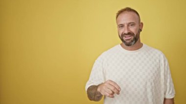 Gülümseyen genç adam, yalıtılmış sarı arka planda yan tarafı işaret ediyor.