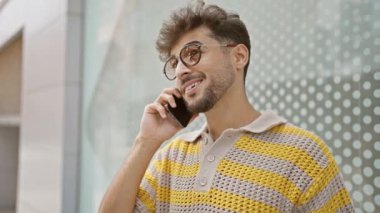 Genç Arap adam gülümsüyor, kendinden emin bir şekilde caddedeki akıllı telefondan konuşuyor.