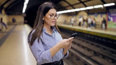 Madrid metro istasyonunda akıllı telefon kullanan güzel İspanyol bir kadın metroda bekliyor.