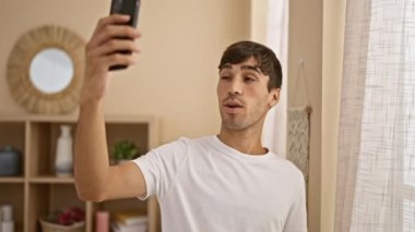 Neşeli, genç İspanyol bir adam akıllı telefonuyla canlı bir video görüşmesi yaparken, evinin rahat oturma odasında, dijital iletişimin neşesini yayıyordu..