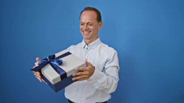 自信に満ちた中年の男性は 喜びに満ちて 彼のサプライズバースデープレゼントを抱きしめ 陽気に微笑みました 白い壁に隔離され 幸福とポジティブさを表現する — ストック動画
