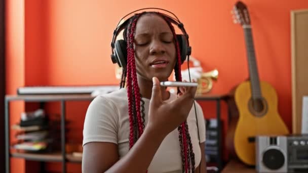 在音乐工作室的中心 美丽的非洲裔美国女音乐家一边拿着智能手机一边唱着一首歌 — 图库视频影像