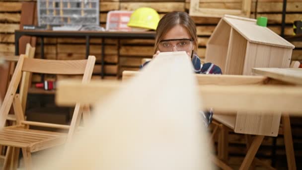 美しく 献身的な若いブロンドの女性大工は 彼女の魅惑的なカーペントリースタジオで木片を愛情を込めて見ています — ストック動画