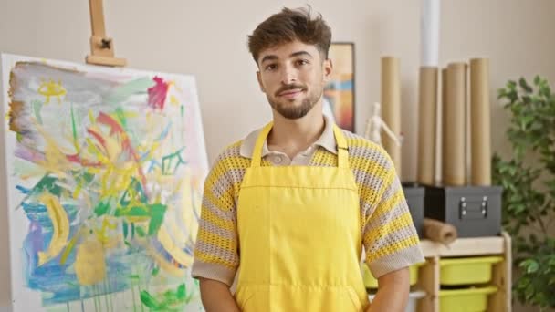 年轻自信的阿拉伯男子 双臂交叉 微笑着在艺术工作室里的画布 一位英俊的艺术家站在他的室内绘画课上感到自豪 — 图库视频影像