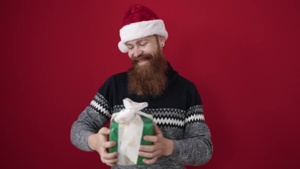 Молодий Рудий Чоловік Тримає Подарунок Різдвяному Капелюсі Над Ізольованим Червоним — стокове відео