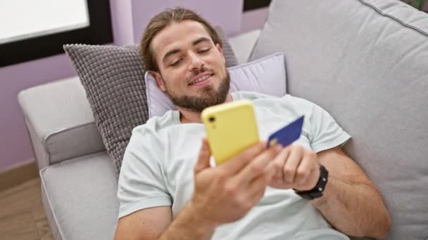 Młody Hiszpan Robi Zakupy Smartfonem Kartą Kredytową Leżącą Kanapie Domu — Wideo stockowe